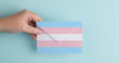 A hand holding an envelope in the colours of trans flag